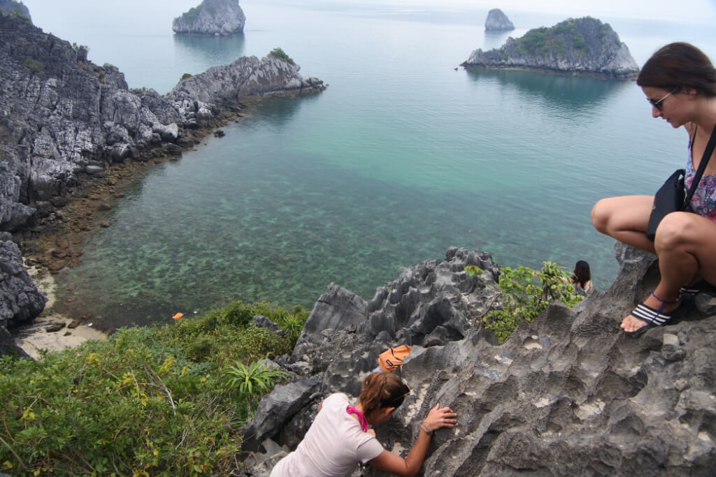 Auf einem Aussichtspunkt in der Halongbucht sitzt eine junge Frau, eine zweite klettert an den Felsen zu ihr hoch