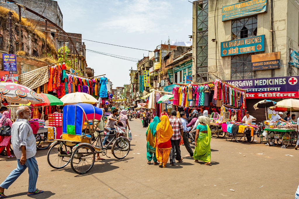 Eine bunte, belebte Straße mit bunten Saris, Rikscha und vielen Shops