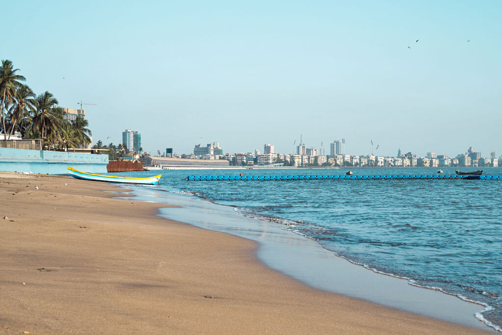 Ein Strand mit einem Boot, im Hintergrund die Skyline von Mumbai