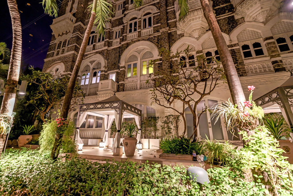 Ein Hotelgebäude von aussen mit einem Pavillion und Palmen bei Nacht