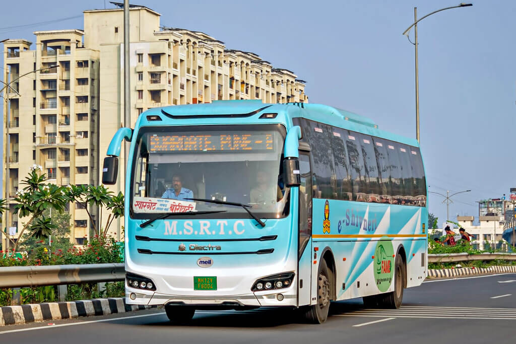 Ein blauer Reisebus fährt auf einer Straße, im Hintergrund Hochhäuser