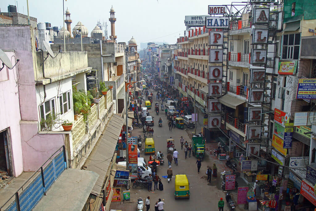 Wuselige Straße eingekesselt von hohen Häuserfassaden und Werbung von Hotels in New-Delhi